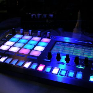 Close-up of an illuminated DJ mixer with vibrant LED pads in a dark studio environment.