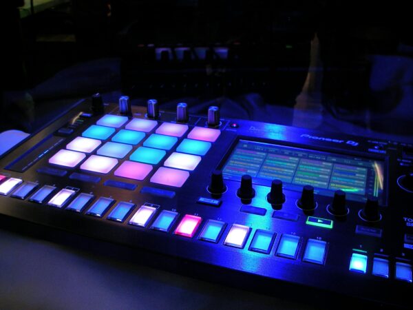 Close-up of an illuminated DJ mixer with vibrant LED pads in a dark studio environment.